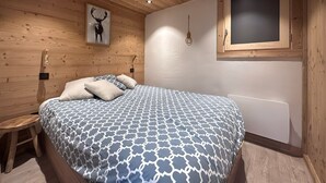 Une chambre avec un plafond en bois, un lit avec une literie à motifs, une lampe fixée au mur et un tableau encadré.