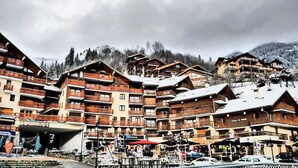 Un ensemble de bâtiments en bois à plusieurs étages, dotés de balcons, qui semblent être un hôtel ou un complexe touristique, se dressant sur fond de montagnes enneigées.