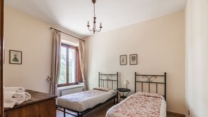 A bedroom with two beds, a wooden dresser, a radiator, and a window with curtains. - Tenuta Pantano Borghese - Apartment 13 (Monte Compatri)