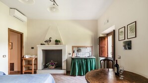 A cozy room with a bed, a wooden table, a fireplace, and a kitchen area. - Tenuta Pantano Borghese - Apartment 14 (Monte Compatri)
