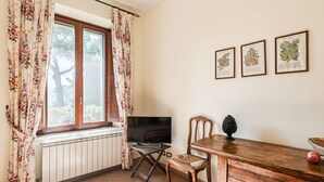 Une pièce chaleureuse avec une table à manger en bois, un téléviseur et une fenêtre ornée de rideaux à motifs floraux.