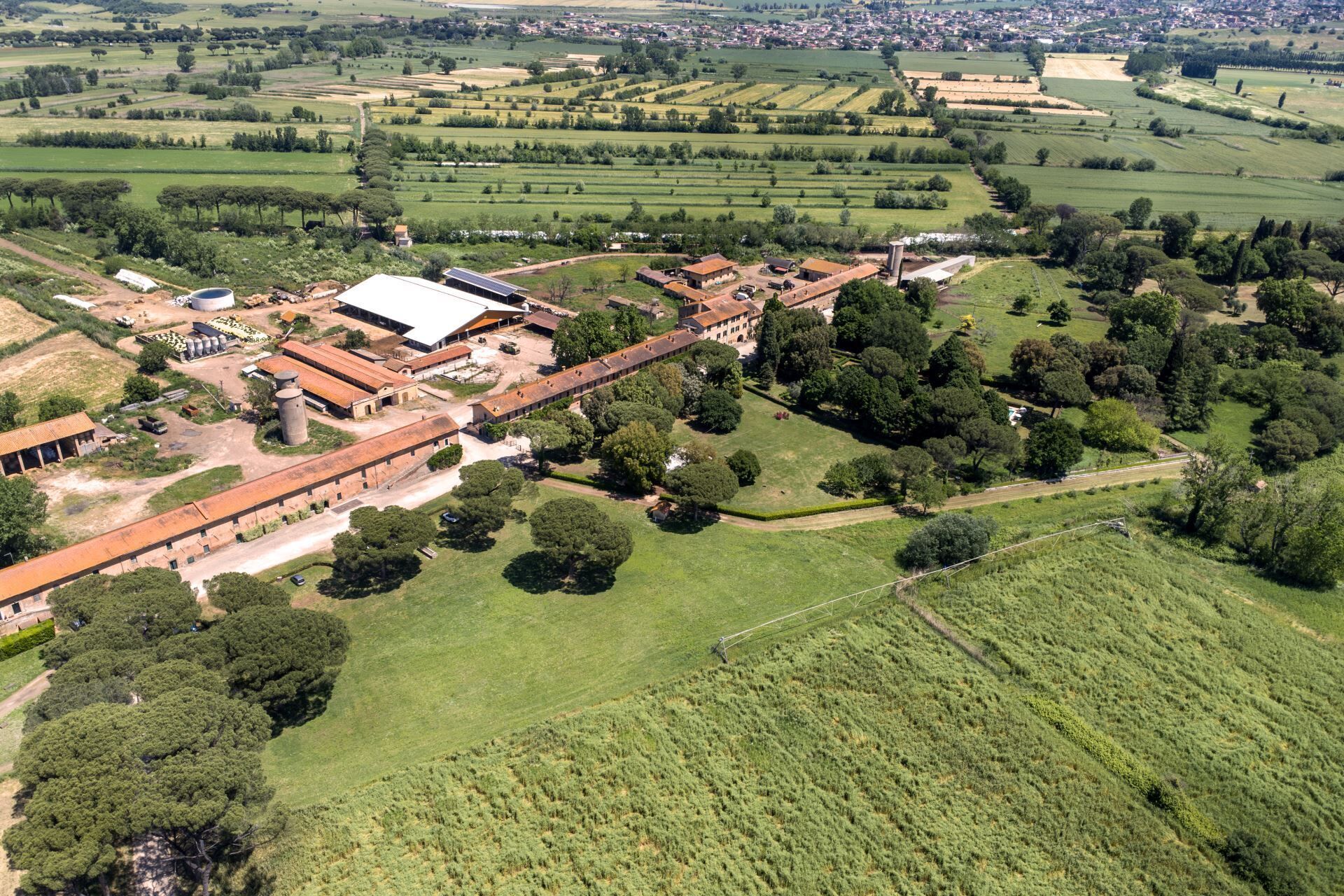 Luchtbeeld van een landgoed op het platteland met meerdere gebouwen, waaronder een grote boerderij, schuren en open velden.