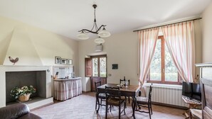 A spacious living area with a fireplace, a dining table with chairs, and a kitchen area with a sink and counter. - Tenuta Pantano Borghese - Apartment 16 (Monte Compatri)