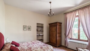 A bedroom with a bed, a wooden wardrobe, a shelf unit, and a window with curtains.