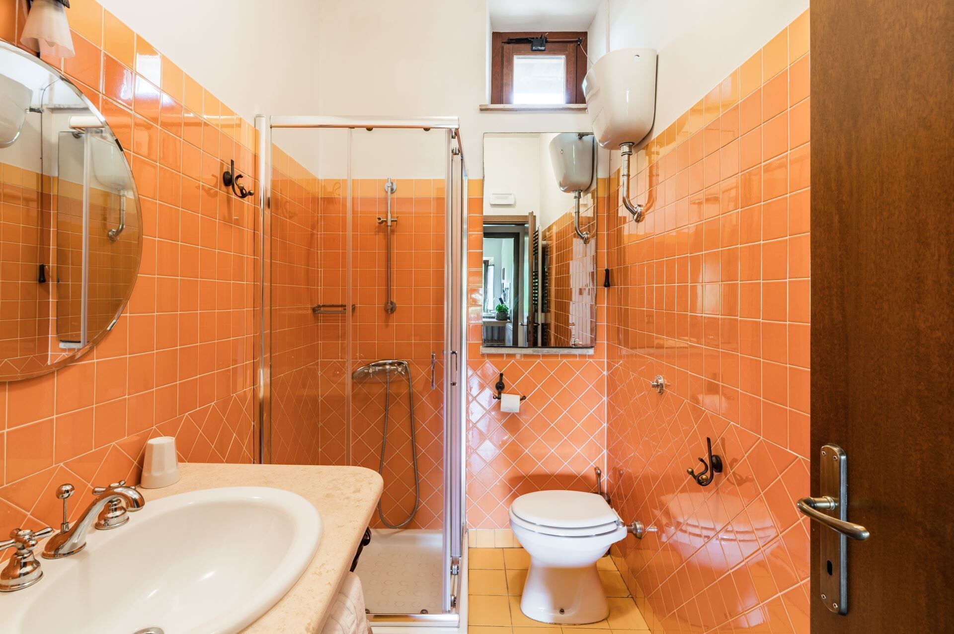 Ein Badezimmer mit orangefarbenen Fliesen, einem weißen Waschbecken, einer Toilette und einer Duschkabine aus Glas.
