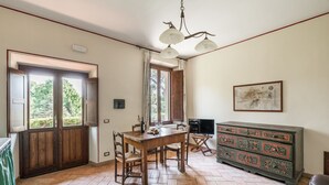A dining area with a wooden table and chairs, a television, and a cabinet with floral designs. - Tenuta Pantano Borghese - Apartment 18 (Monte Compatri)