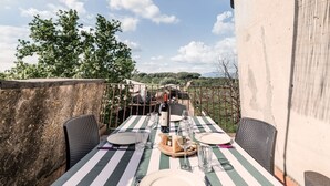 Un área de comedor al aire libre con una mesa dispuesta para dos personas, que incluye un mantel a rayas, platos, cubiertos y una botella de vino.