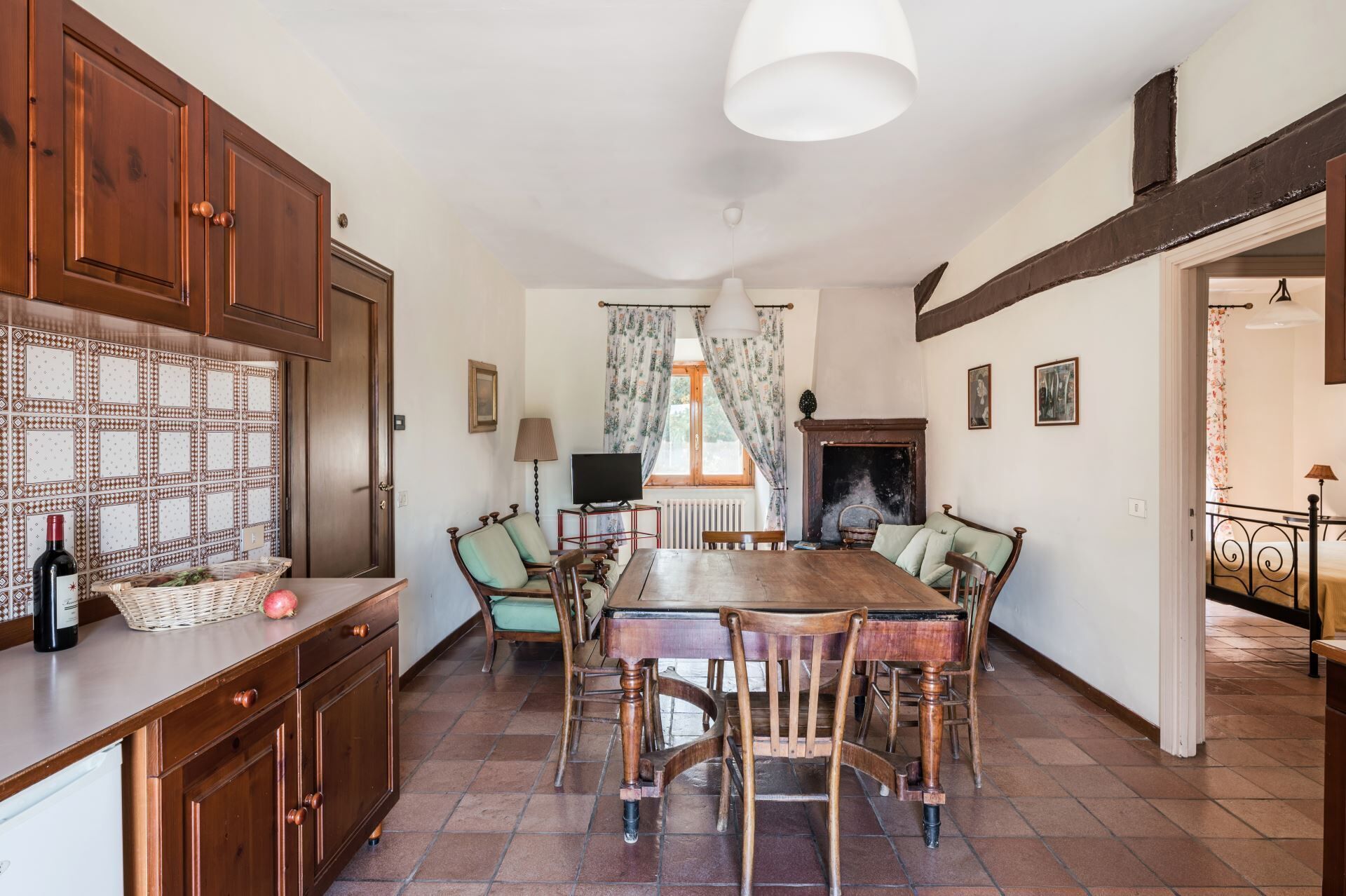 Comedor con mesa de madera, sillas y chimenea. Hay un televisor sobre un mueble bajo y una ventana con cortinas.