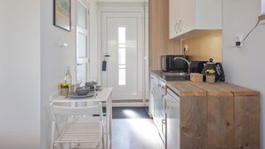 A compact kitchen with white cabinetry, a wooden countertop, a microwave, and a small dining area with a table and chairs. - Forest and Ocean - Perfect couple or friends getaway (Zandvoort)