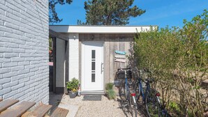 A modern building with a white brick exterior, a wooden door, and a small garden area with a bicycle and potted plants. - Forest and Ocean - Perfect couple or friends getaway (Zandvoort)