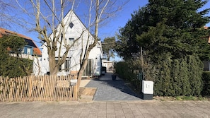 Une rue résidentielle bordée d’une maison blanche, d’une clôture en bois et d’une haie.