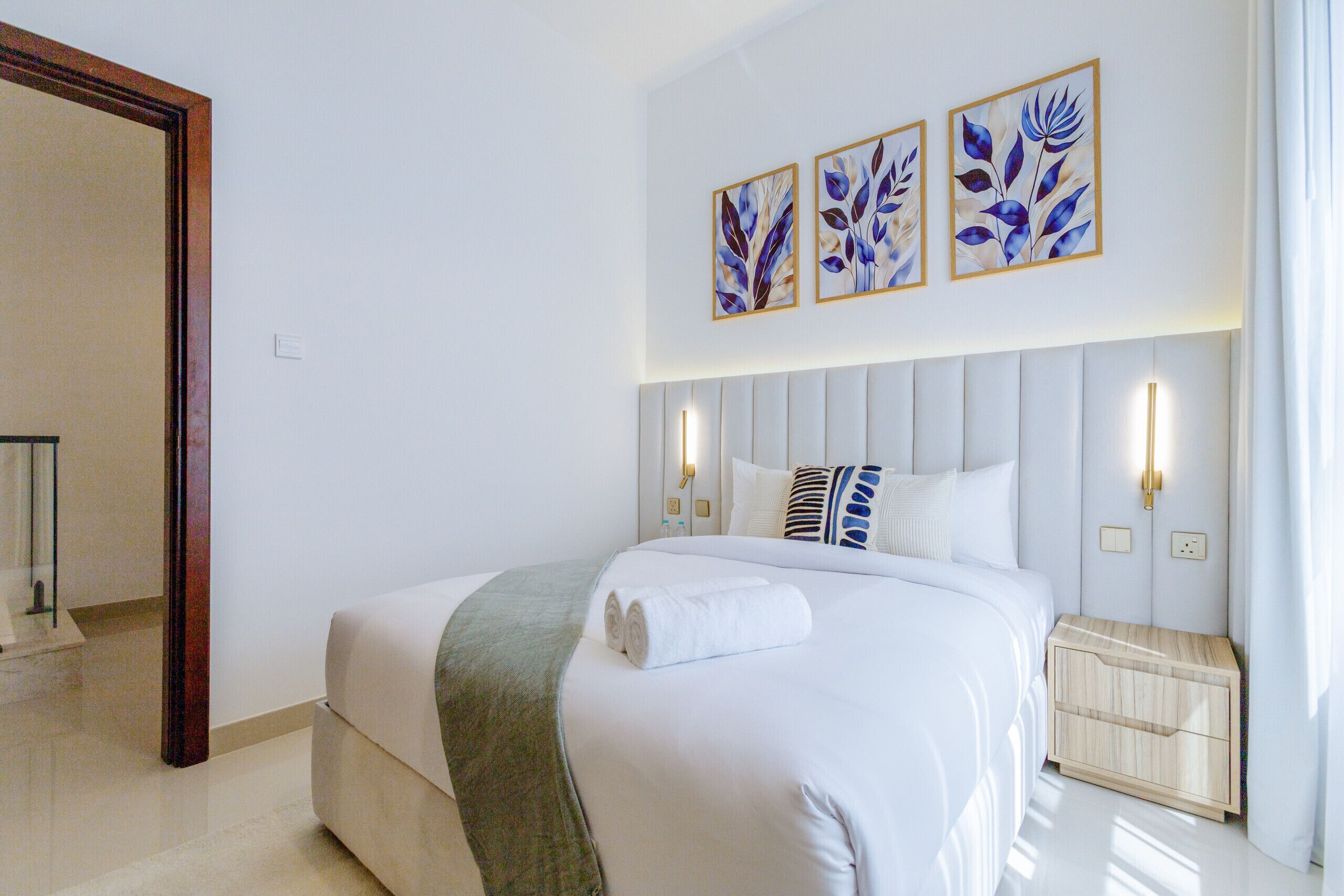 A hotel room with a large bed, a bedside table, a nightstand, and wall-mounted artwork.