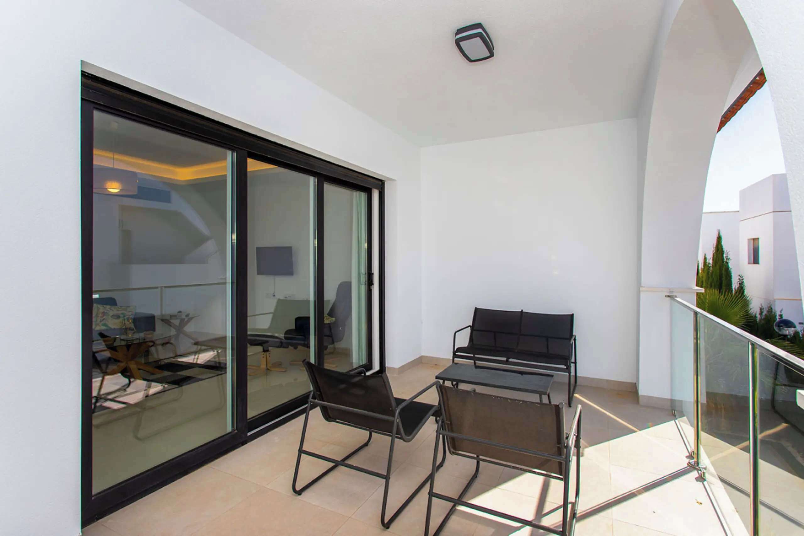 Un balcon avec une porte vitrée donnant sur une pièce, une table en métal avec des chaises et une rambarde.