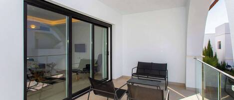 Un balcon avec une porte vitrée donnant sur une pièce, une table en métal avec des chaises et une rambarde.
