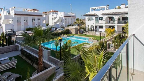 Un quartier résidentiel doté d’une piscine entourée de palmiers, avec un ciel bleu dégagé.
