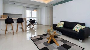 Un salon moderne avec un canapé noir, deux fauteuils noirs, une table basse en verre et un tapis à carreaux.
