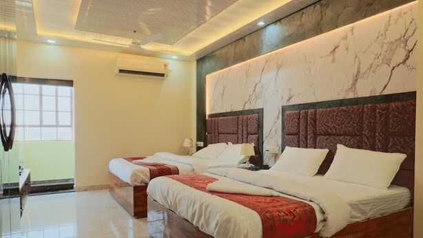 Habitación de hotel con dos camas, pared de mármol, ventilador de techo y ventana con cortinas.