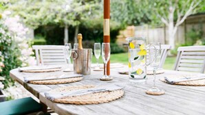 Une table en bois, installée à l’extérieur, avec une carafe, des verres et une bouteille.