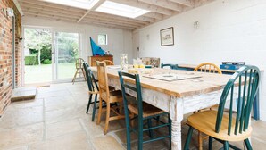 Un coin repas avec une table et des chaises en bois, un mur en briques et une vue sur le jardin grâce à des portes vitrées.