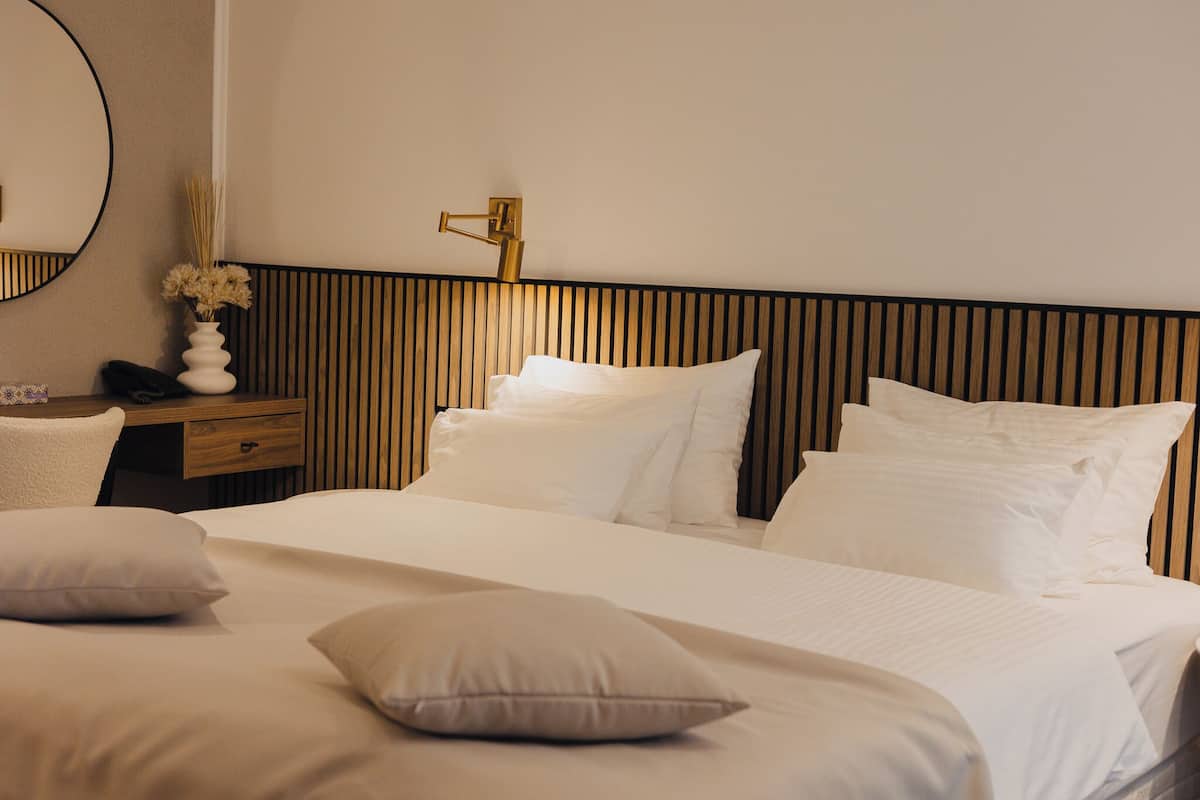Une chambre d’hôtel avec un grand lit, une table de chevet avec une lampe, un miroir et un vase contenant des fleurs séchées.