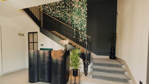 A modern reception area with a curved black desk, a potted plant, and a staircase with a floral wall design. - Hotel Flaneur (Belgrade)