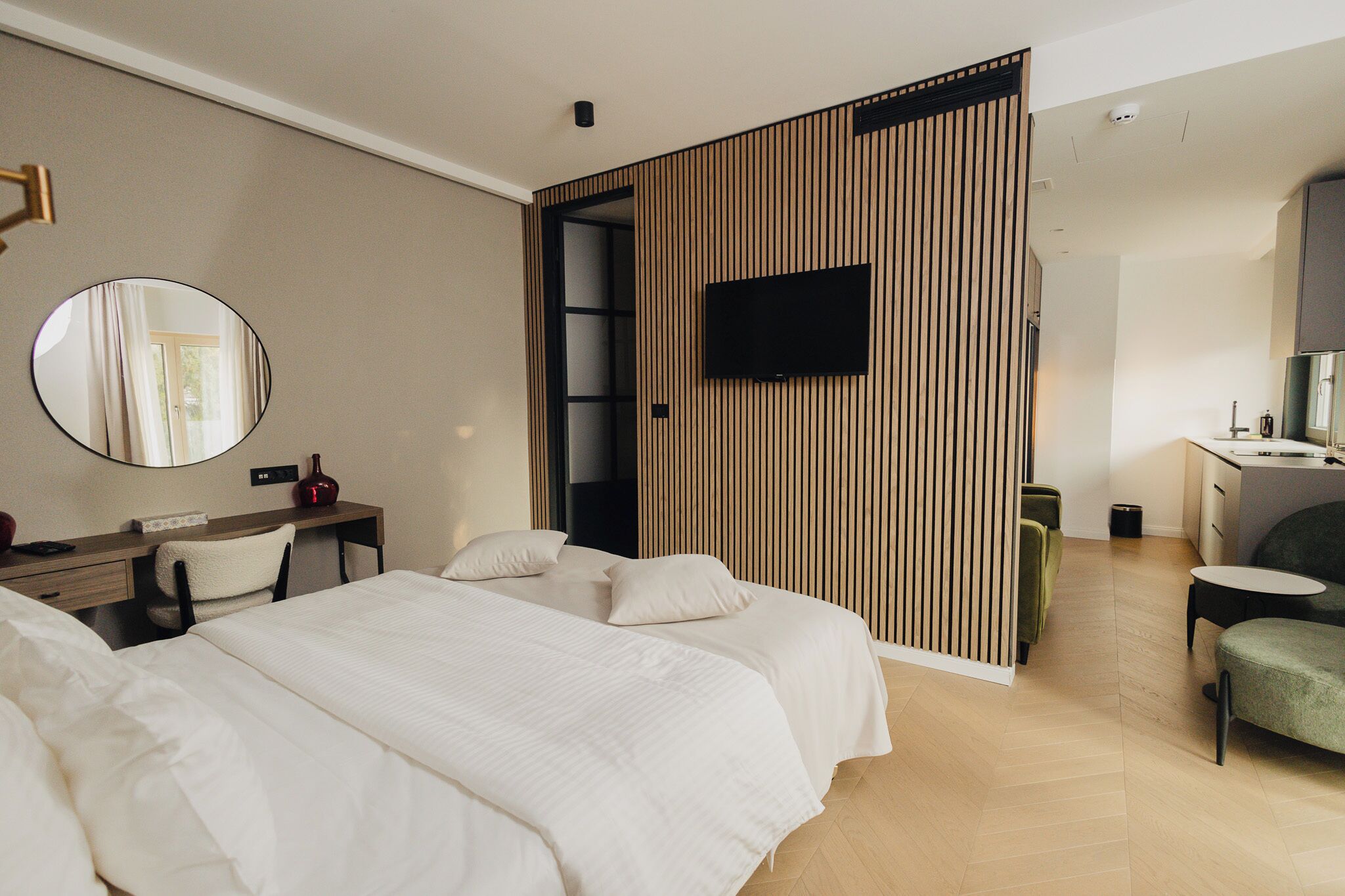 A modern hotel room with a large bed, a desk with a chair, a television mounted on the wall, and a small seating area with a table and chairs.