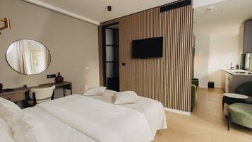 A modern hotel room with a large bed, a desk with a chair, a television mounted on the wall, and a small seating area with a table and chairs.