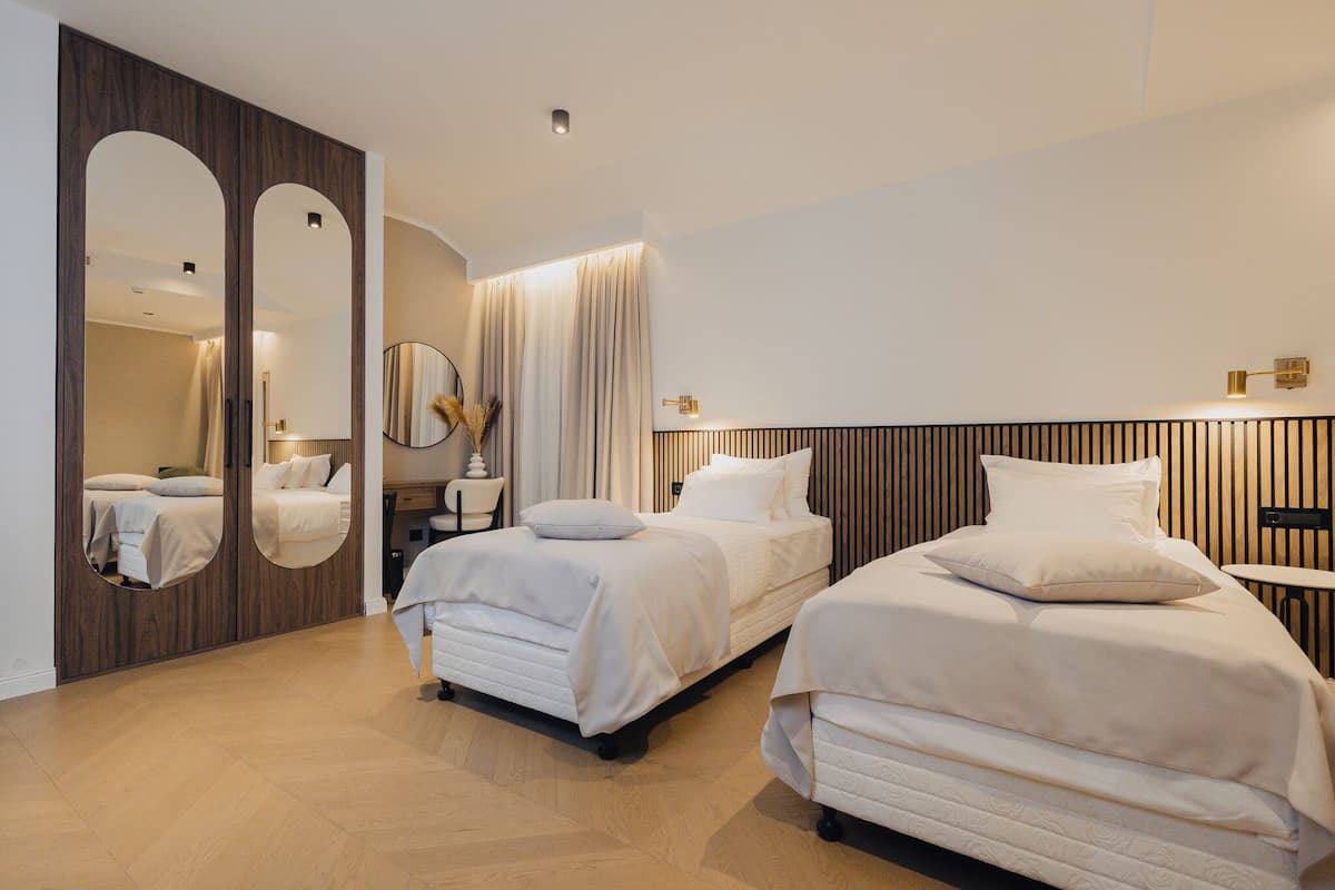 Une chambre d’hôtel moderne avec deux lits, un grand miroir, une coiffeuse avec un miroir et une petite table.