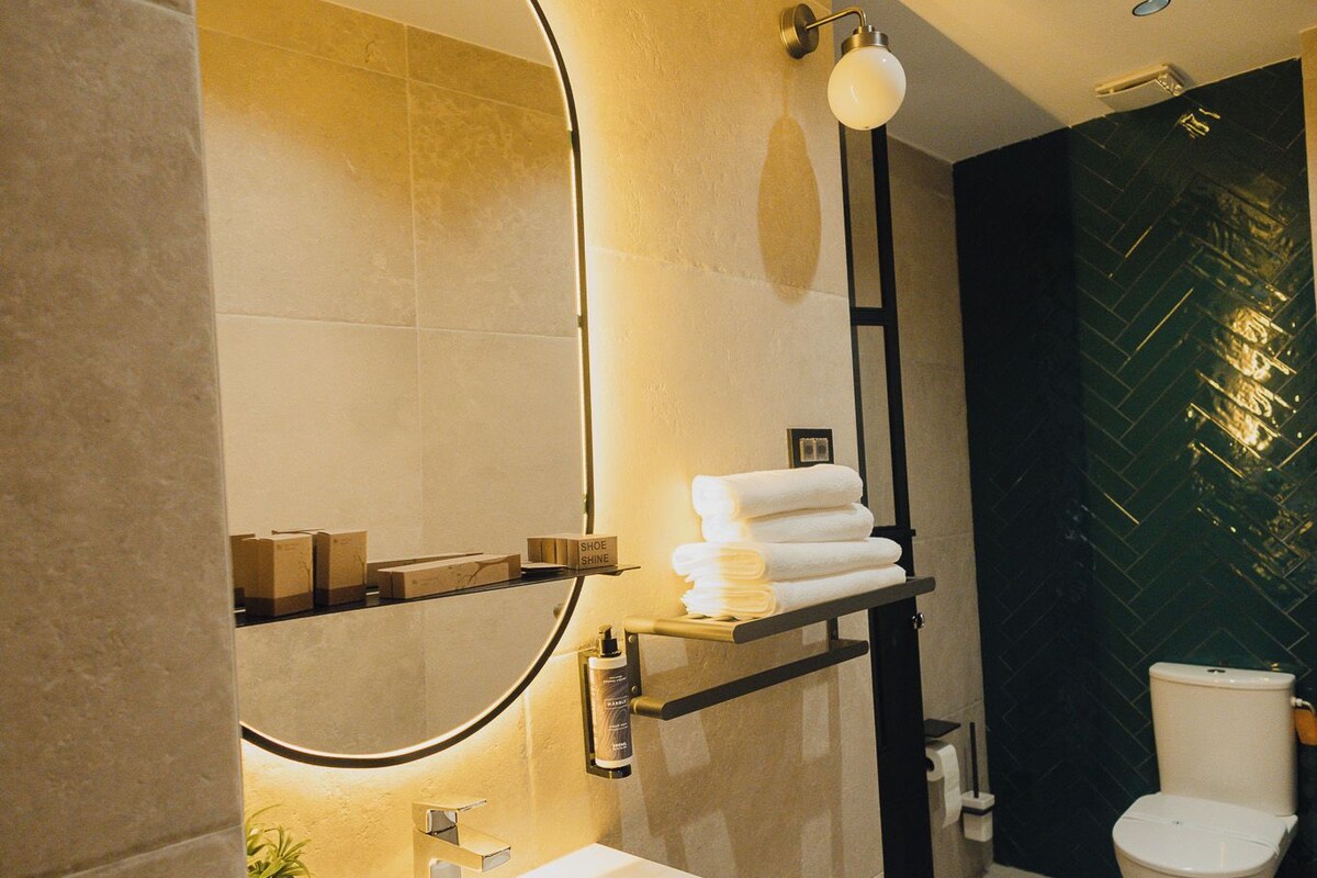 A modern bathroom with a large mirror, a sink, a toilet, and a shelf with towels.