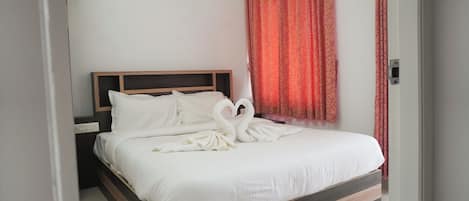 Una cama bien hecha con sábanas blancas y una toalla dispuesta en forma de corazón.