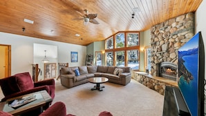 A cozy living room with a stone fireplace, a large TV, and a wooden ceiling.