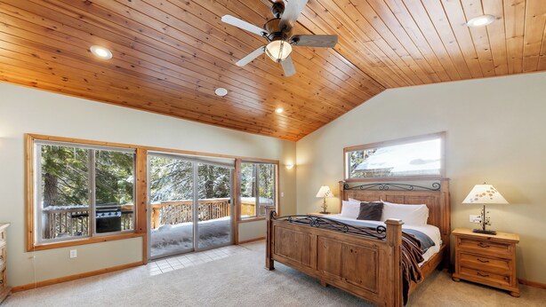 A bedroom with a wooden ceiling, large windows, a bed, a nightstand, and a ceiling fan.