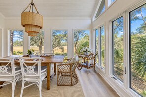 A dining area with a wooden table, white wicker chairs, and a hanging light fixture.