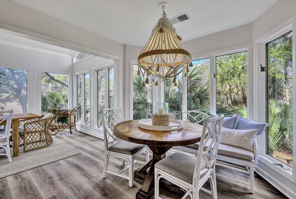 A spacious room with a round wooden table, white wicker chairs, and a large window with a view of greenery. - 45 Stoney Creek – Your Ideal Hilton Head Retreat w/ Private Beach Parking! (Hilton Head Island)