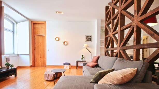 Een moderne woonkamer met een grijze bank, houten details en een groot raam dat natuurlijk licht binnenlaat.