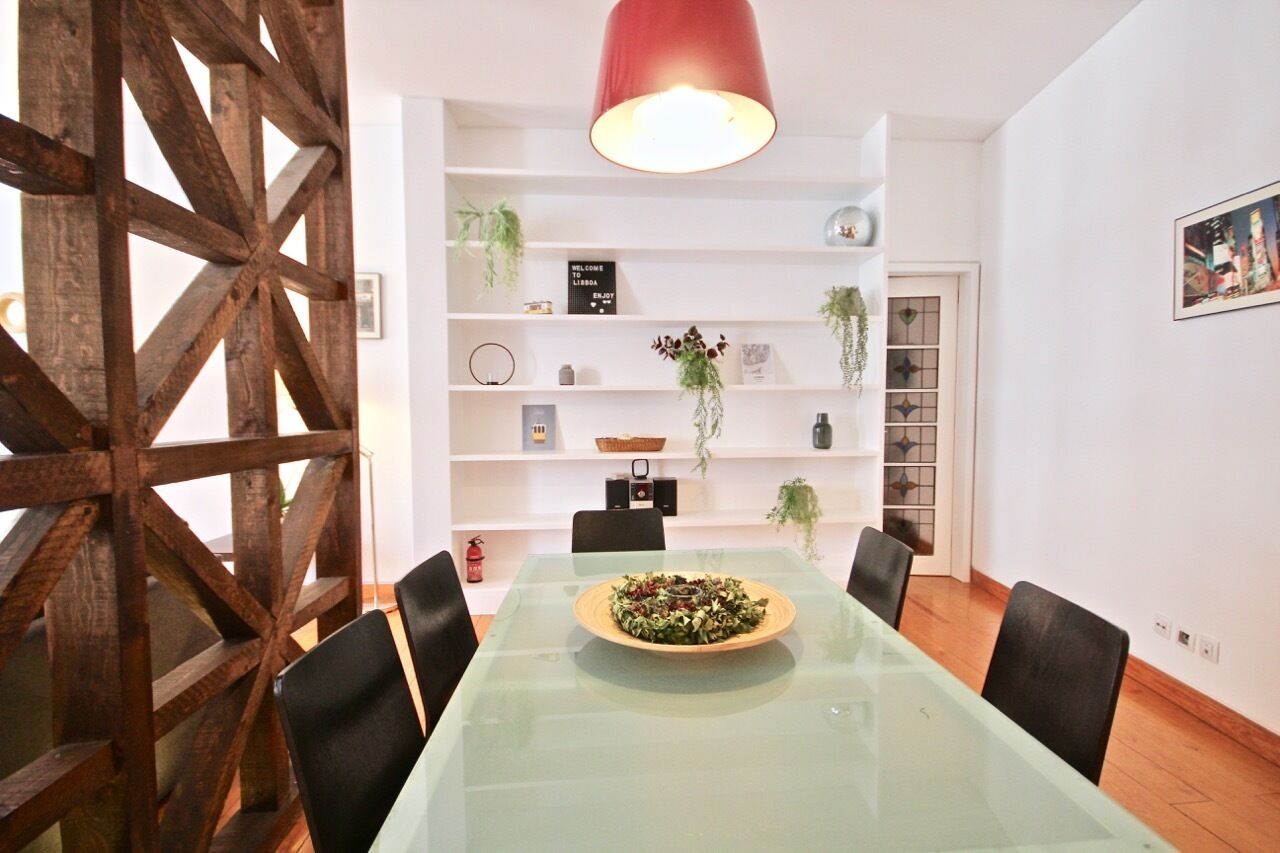 Un coin repas comprenant une table en verre, des chaises noires, un buffet en bois avec des étagères et un luminaire suspendu rouge.