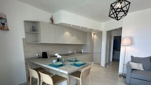 Una cucina moderna con zona pranzo, pavimento in legno chiaro e un divano grigio nel soggiorno.