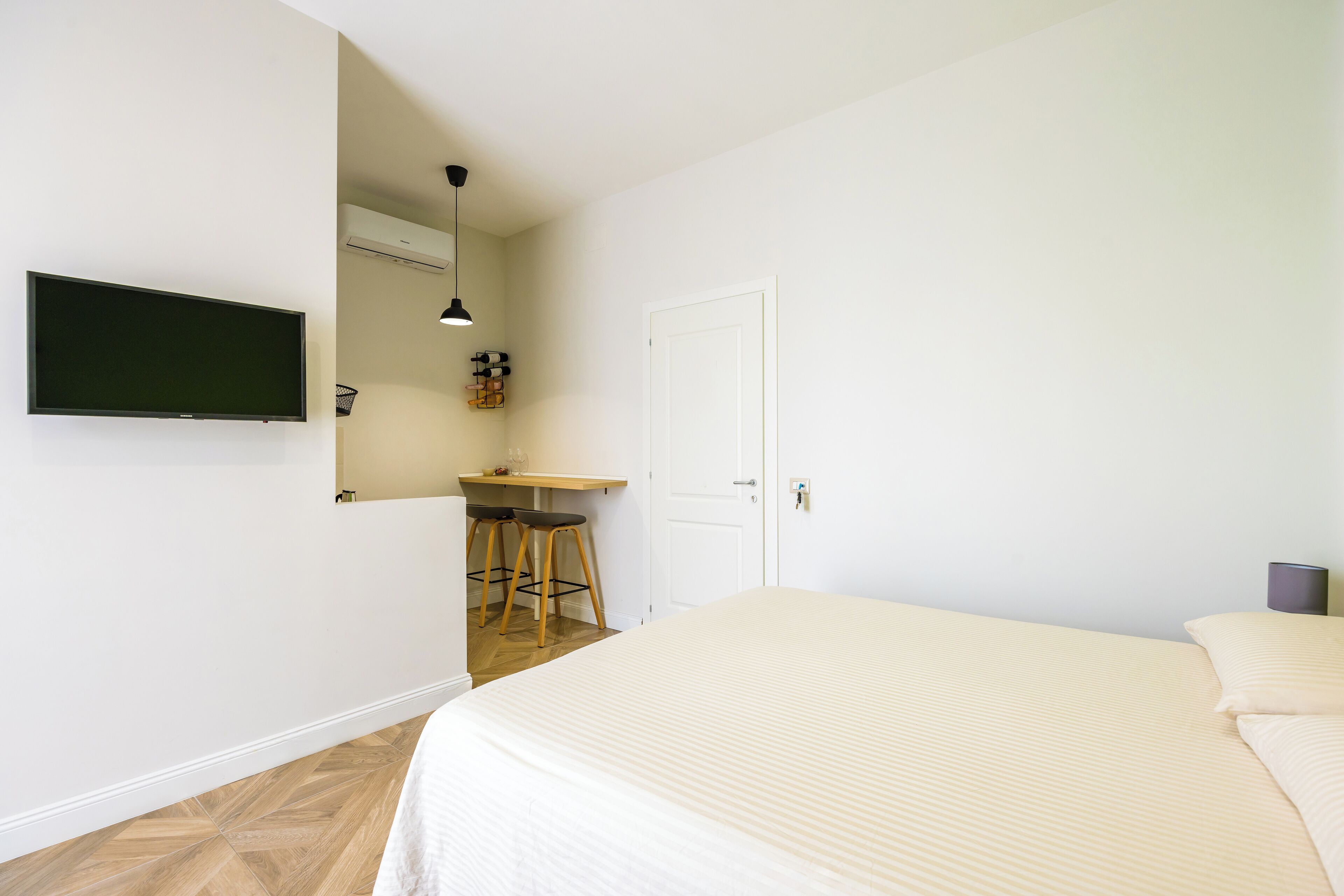 A bedroom with a bed, a desk with two chairs, a television, and a door.