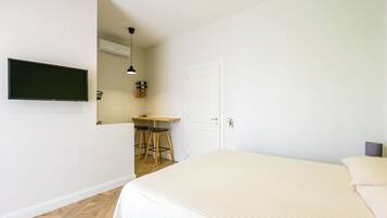 A bedroom with a bed, a desk with two chairs, a television, and a door.