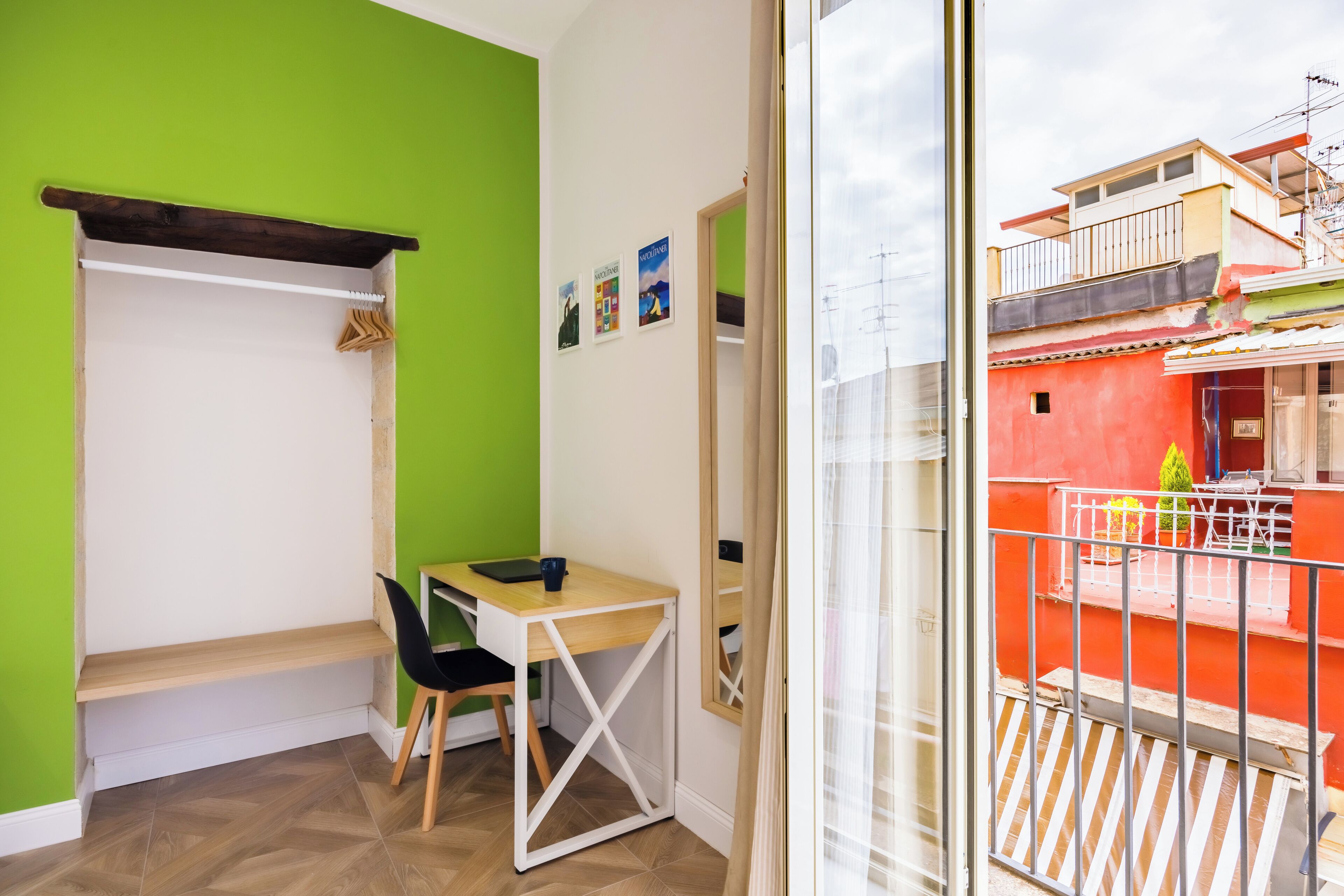 Una habitación con pared verde, un escritorio de madera, una silla negra y una ventana pequeña.