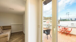 A room with a sofa, a sliding glass door leading to an outdoor patio with a table and chairs. - Terrazza Terzo Cardine (Naples)
