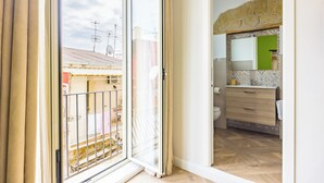 A room with a sliding glass door leading to a balcony, a bathroom with a green-tiled wall, and a wooden floor. - Terrazza Terzo Cardine (Naples)
