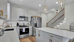 Une cuisine moderne dotée d’appareils électroménagers en acier inoxydable, de meubles blancs et d’un escalier en bois.