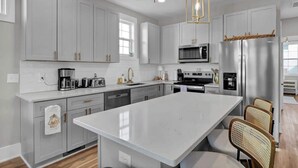 Une cuisine moderne avec des meubles blancs, un grand îlot central, des appareils en acier inoxydable et des chaises en osier.