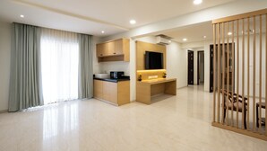 A modern hotel room with a kitchen area, a seating area with a TV, and a view of the outside through large windows.