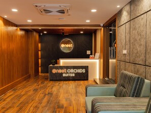 A reception area with a wooden floor, a reception desk labeled "Nest Orchids Suites," and a seating area with a striped cushion. - Atnest Orchids Suites (Hyderabad)