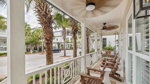 A covered outdoor area with wooden benches and a railing, palm trees, and a view of a street with buildings. - Tranquil Shores | Walk to Beach | Largest 30A Pool | Sleeps 12 | 6 Bikes (Panama City Beach)