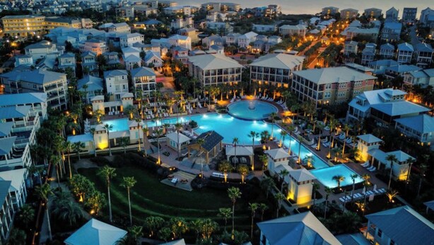 A resort with a central pool, multiple buildings, and a view of the ocean at dusk. - Tranquil Shores | Walk to Beach | Largest 30A Pool | Sleeps 12 | 6 Bikes (Panama City Beach)