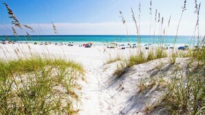A sandy beach path leading to the ocean with beach umbrellas and people in the distance. - Tranquil Shores | Walk to Beach | Largest 30A Pool | Sleeps 12 | 6 Bikes (Panama City Beach)