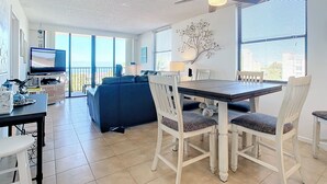 Un salon moderne comprenant un coin repas, un ventilateur de plafond, de grandes fenêtres et un téléviseur.